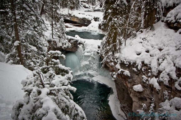 winter view of cascading pools of water with snow covered trees in johnston canyon