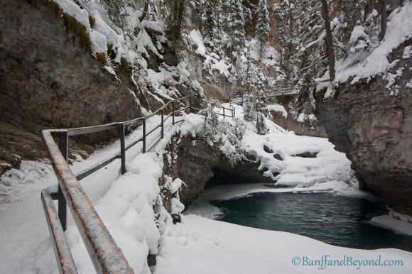 winter hike in johnston canyon on snow covered catwalk going past aqua colored water