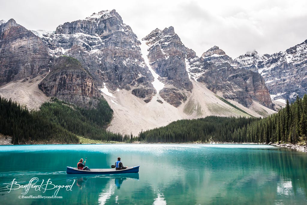 a canoe on the turquoise blue water of moraine lake with the mountain in the background