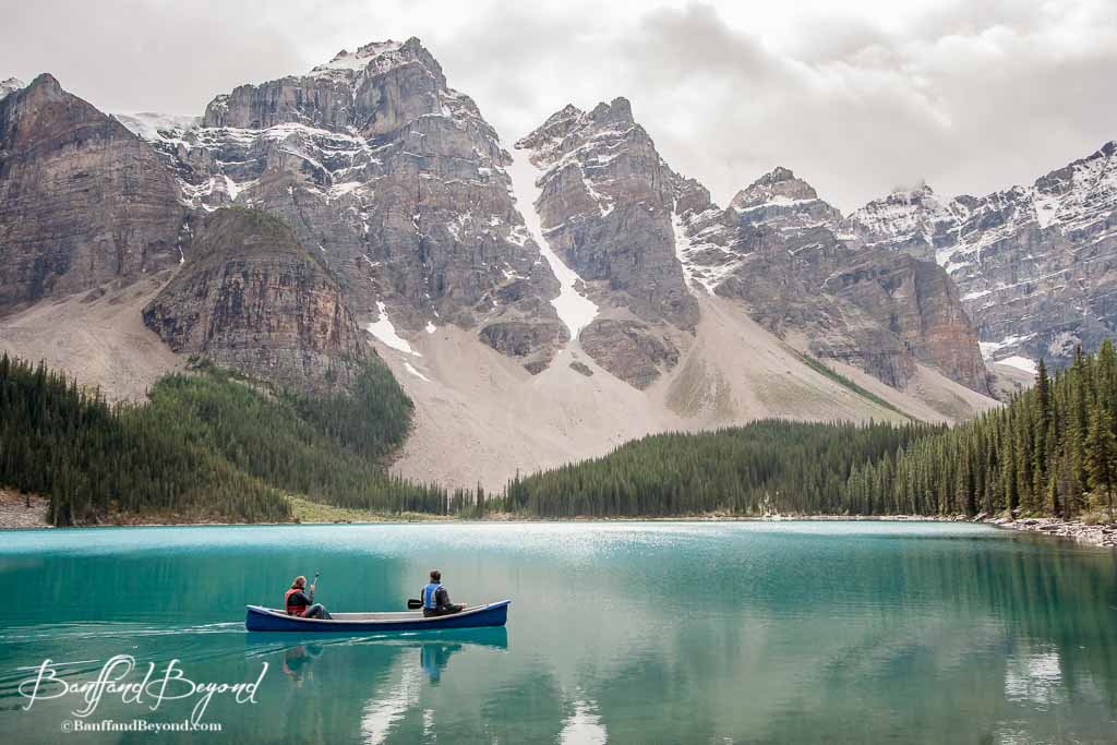 two people in a canoe on the turquoise water of moraine lake with the mountains in the background