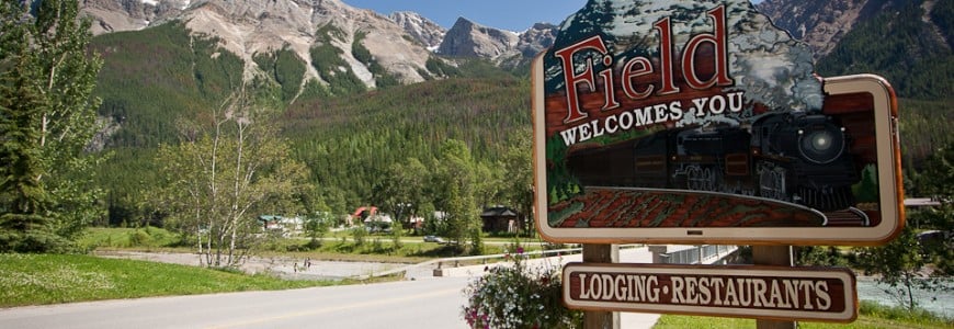 field-welcomes-you-sign-lodging-restaurants-groceries-crafts-mountains-road-trees-town-yoho-national-park-british-columbia